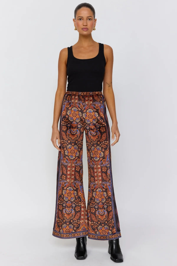 Woman wearing a black tank top and patterned pants on a white background