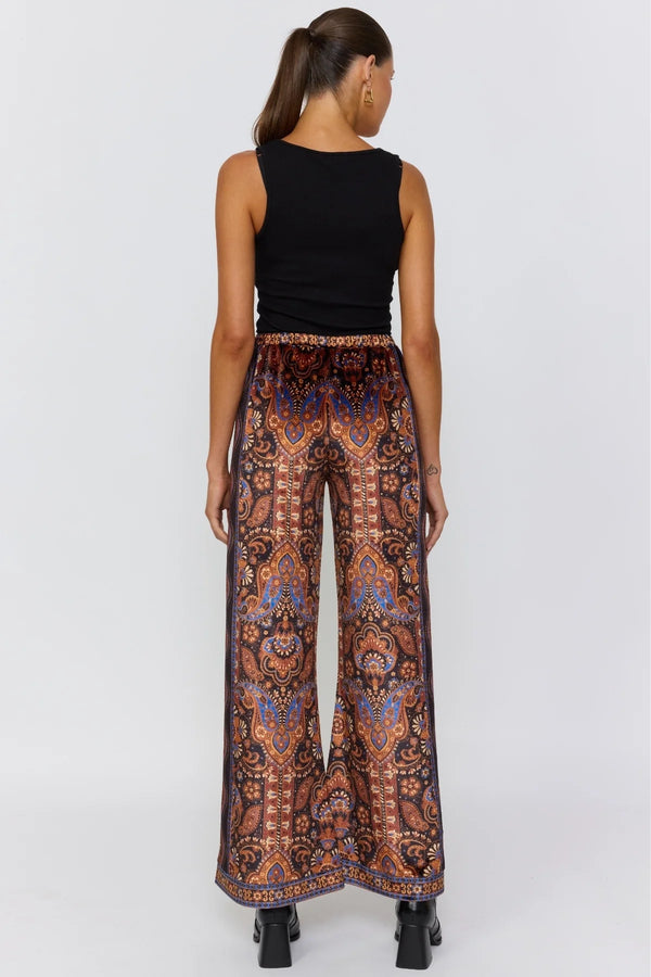 Woman wearing a black sleeveless top and patterned pants on a white background