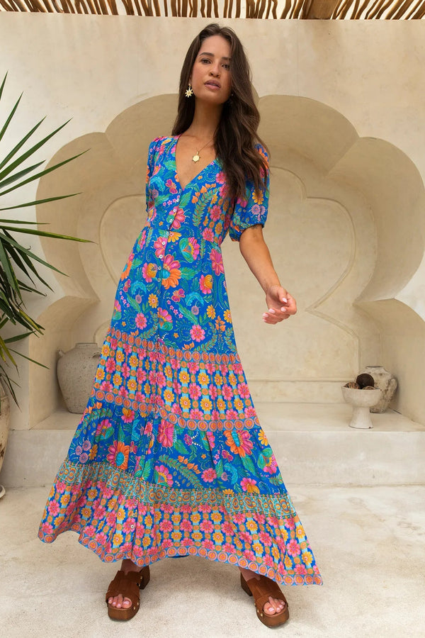 Woman wearing a colorful floral dress standing in a decorative outdoor setting.