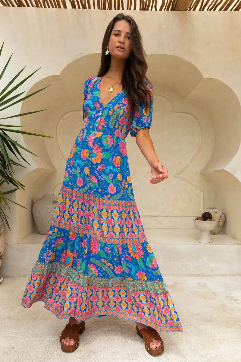 Woman wearing a colorful floral dress standing in a decorative outdoor setting.