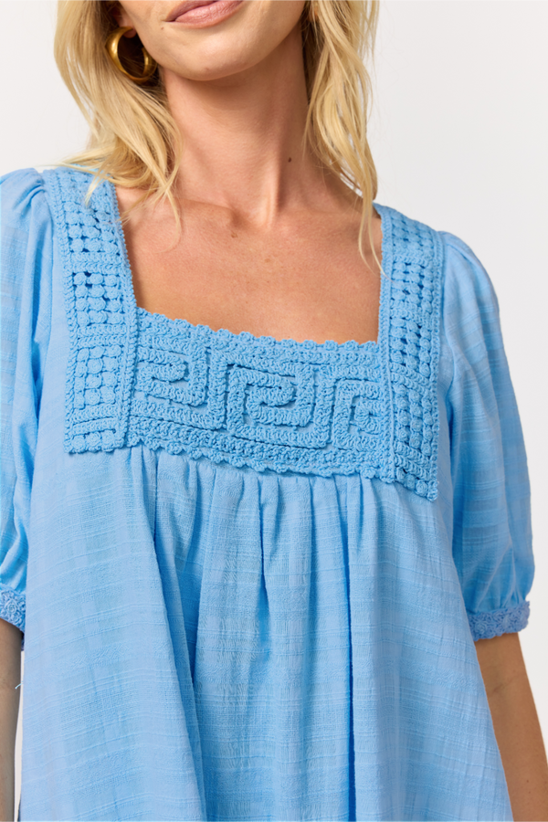 Close-up of a light blue cotton babydoll dress showing the crochet-trimmed square neckline and gathered puff sleeves.