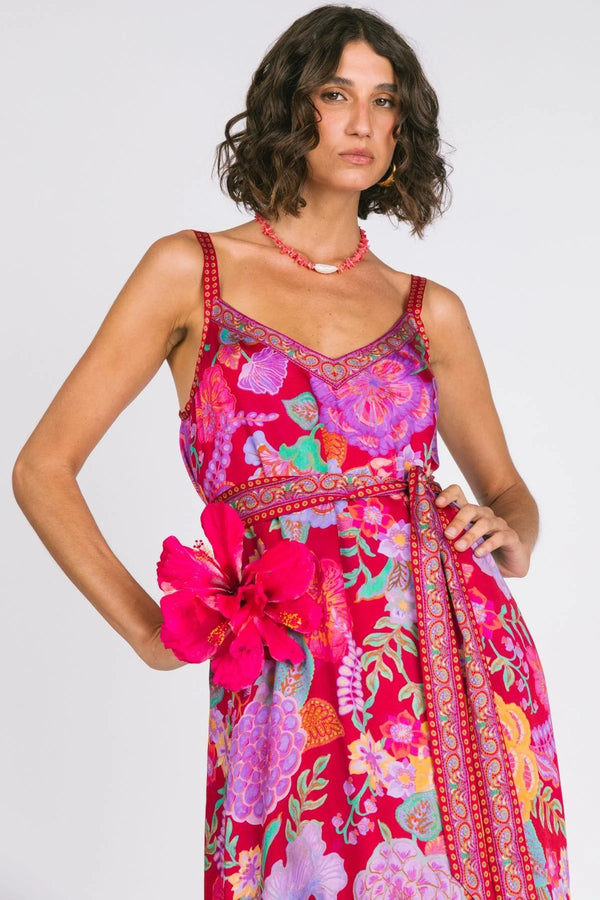 Woman wearing a colorful floral dress with a pink flower accessory on a white background