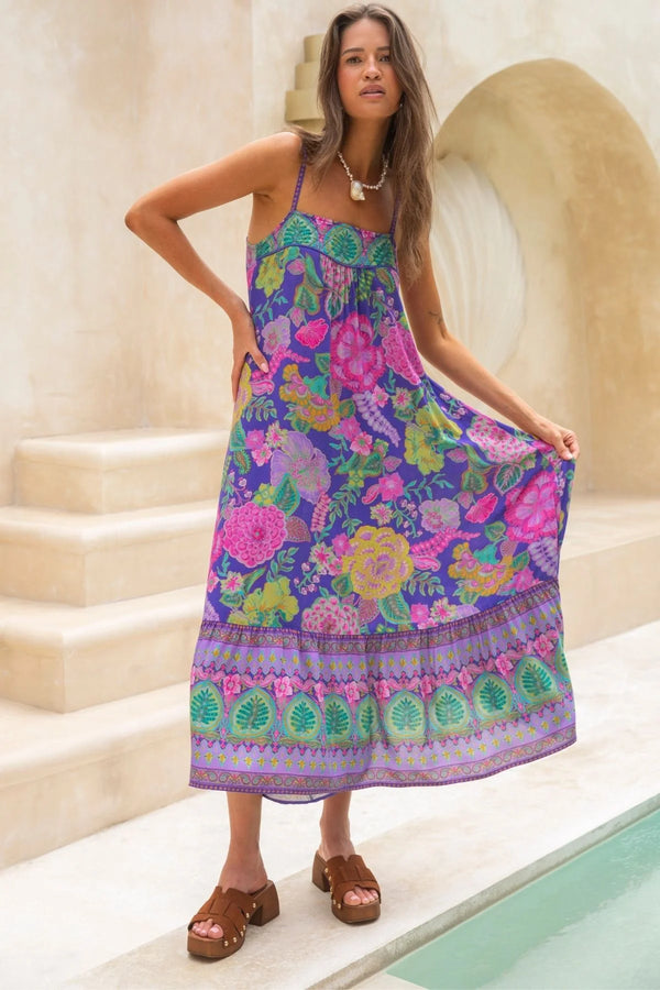 Woman wearing a colorful floral dress standing in front of a stone wall.