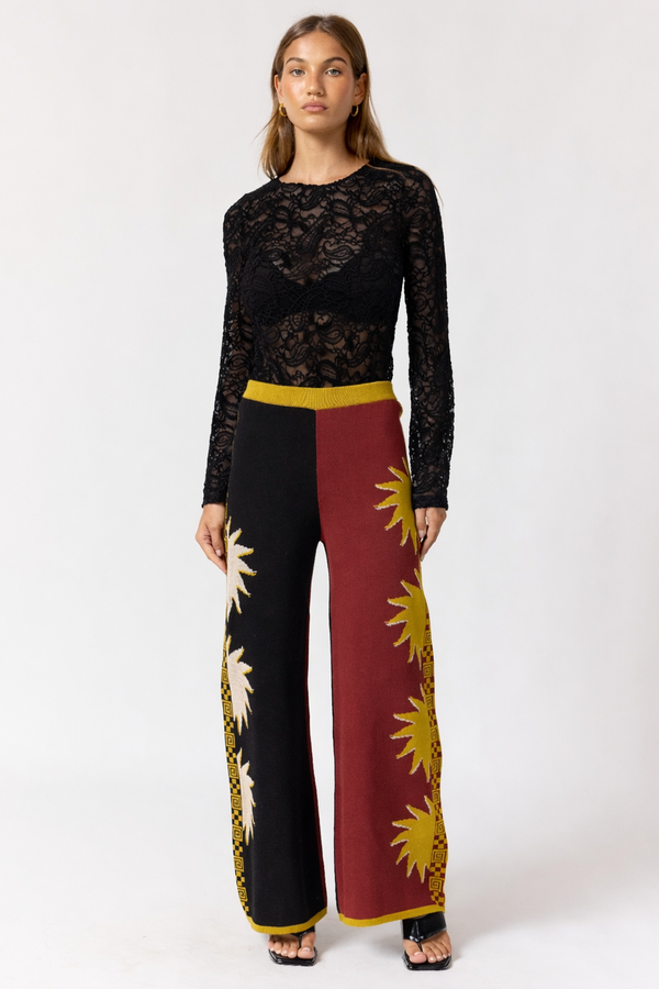 Woman wearing a black lace top and colorful pants on a white background