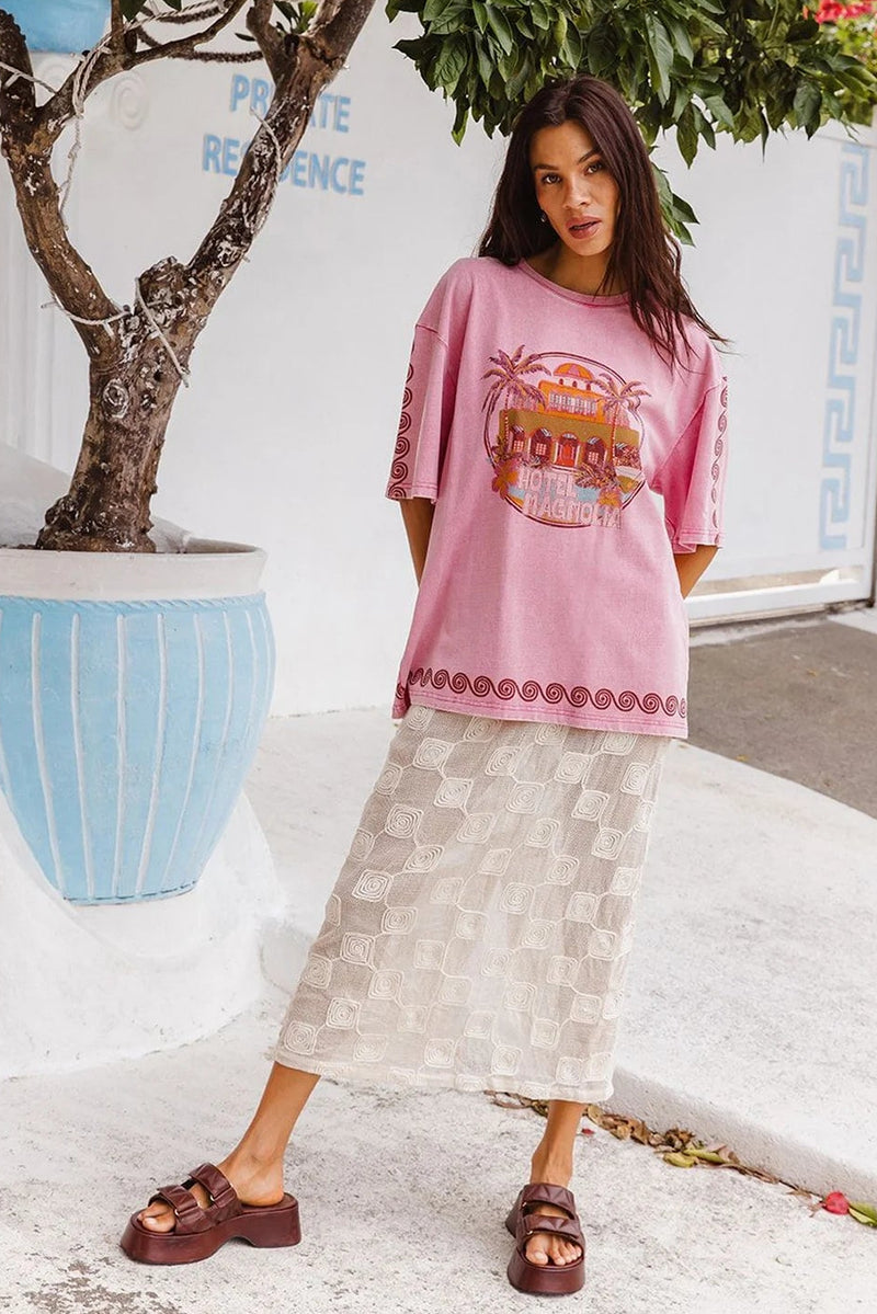 Woman wearing a pink graphic t-shirt and patterned skirt standing outdoors.