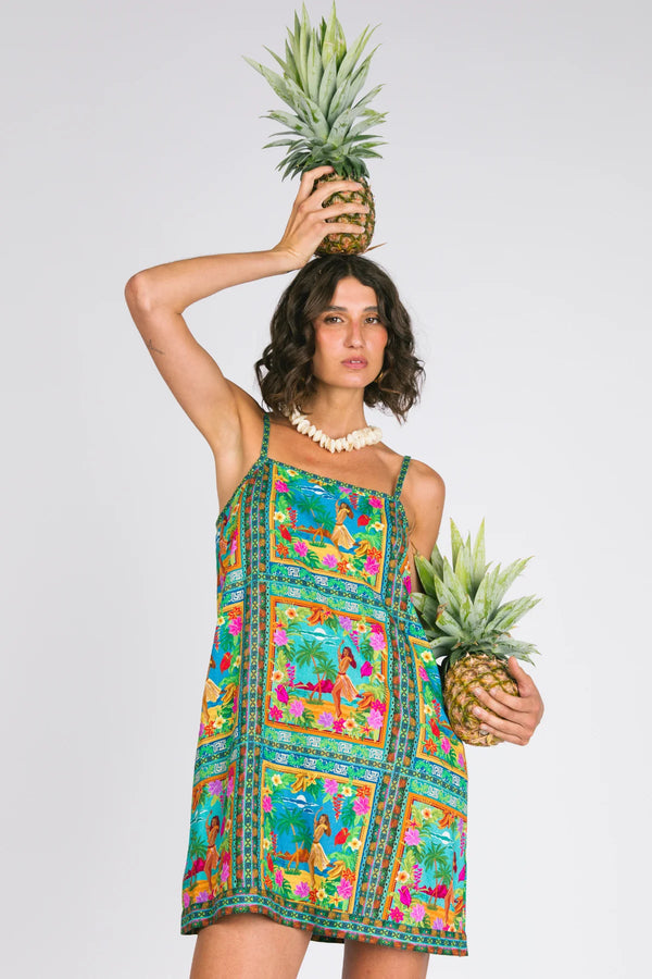 Woman in a colorful dress holding a pineapple against a plain background