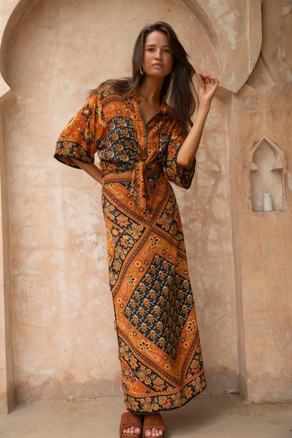 Woman wearing a patterned dress standing in front of an arched stone wall.