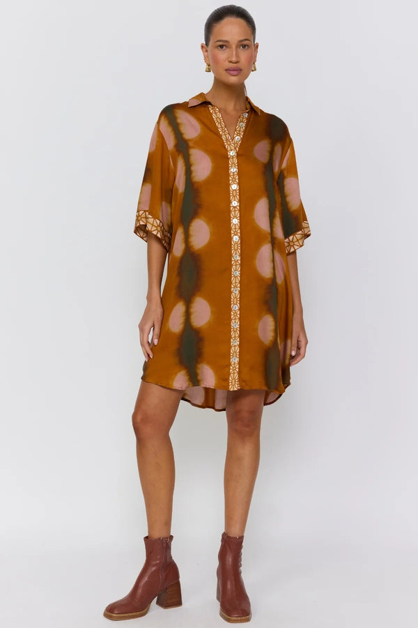 Woman wearing a brown polka dot dress with gold accents on a white background