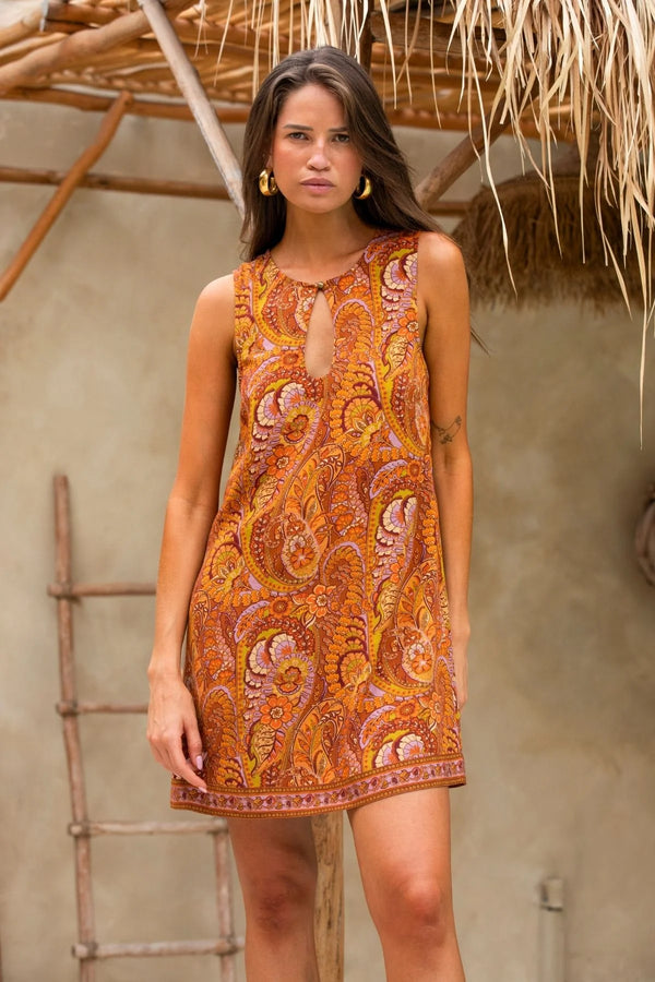 Woman wearing a patterned dress standing in front of a textured wall with a ladder.