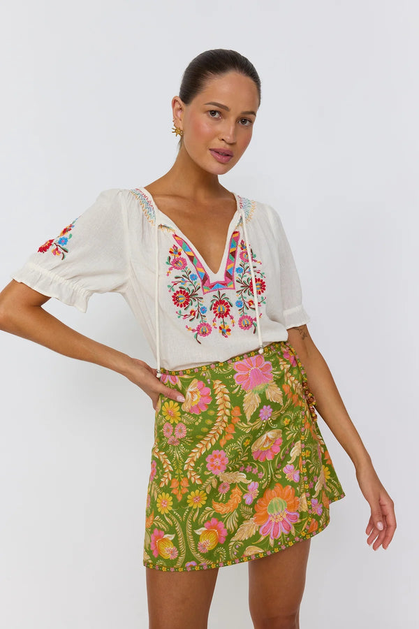 Woman wearing a white blouse with floral embroidery and a green skirt with floral pattern on a white background