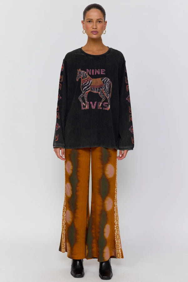 Person wearing a black sweater with a horse graphic and text, paired with brown patterned pants on a white background