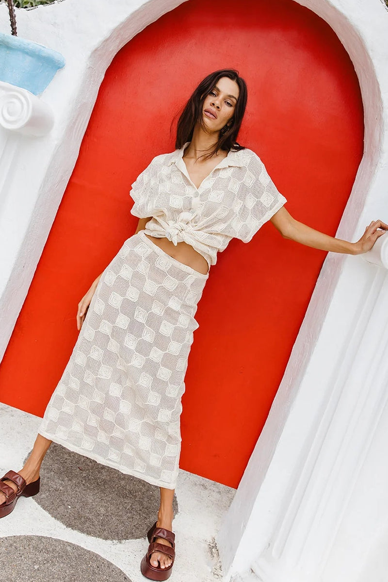 Woman in a white outfit standing in front of a red door with white archway