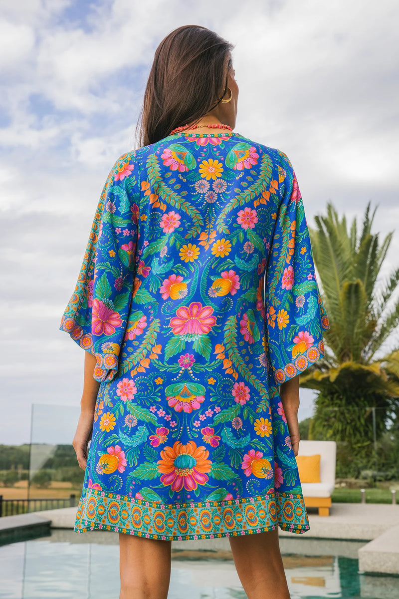 Woman wearing a colorful floral dress with a pool and palm trees in the background