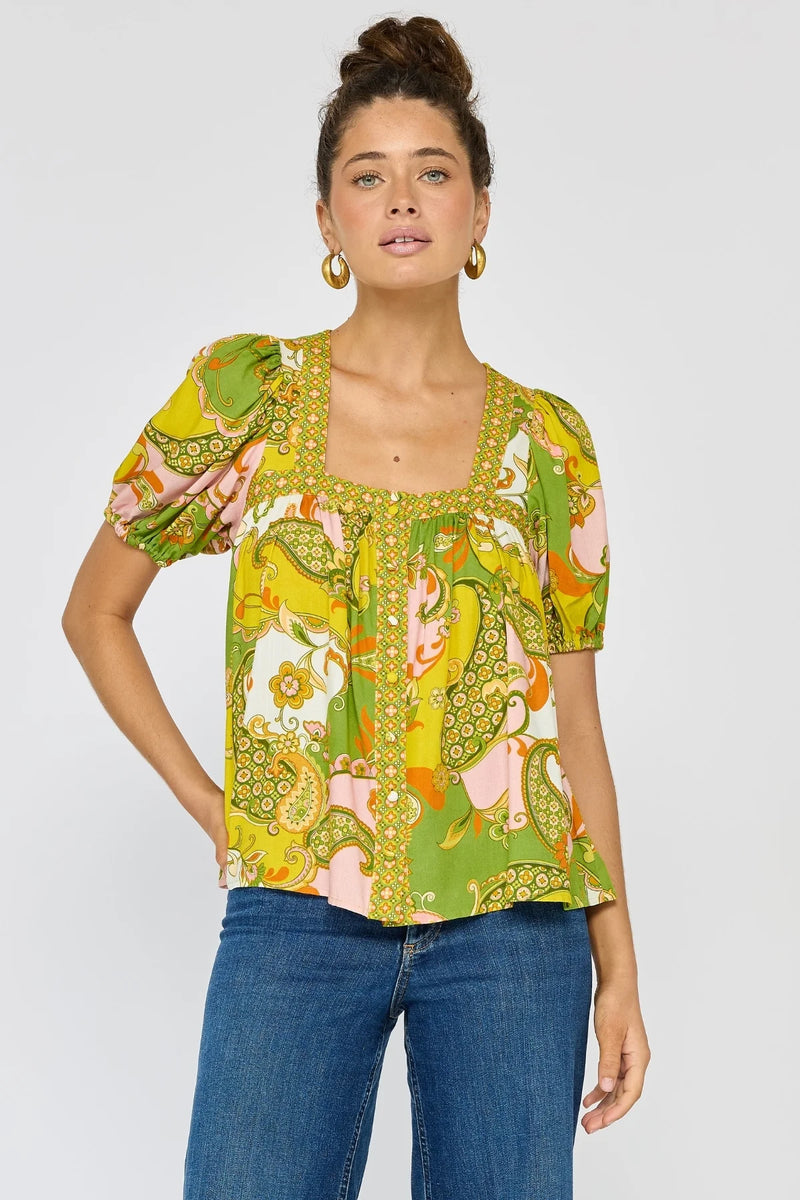 Woman wearing a colorful patterned top and blue jeans on a white background