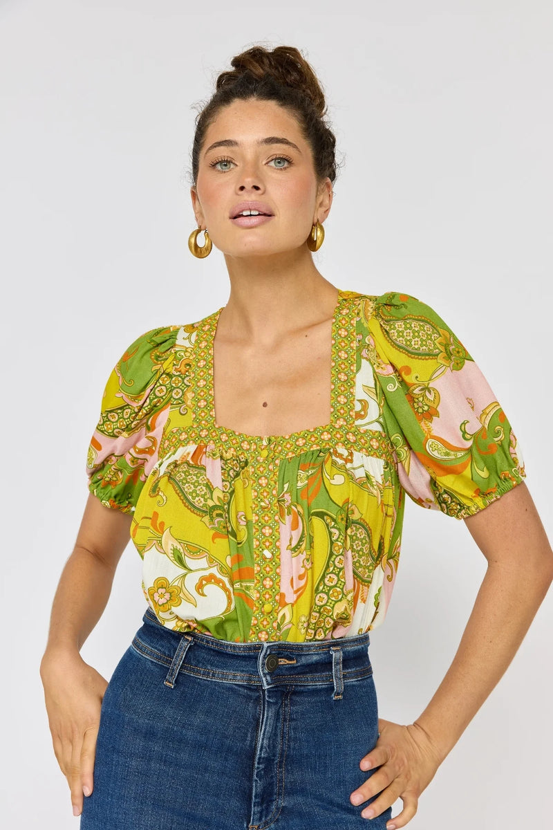 Woman wearing a colorful patterned top and blue jeans on a white background