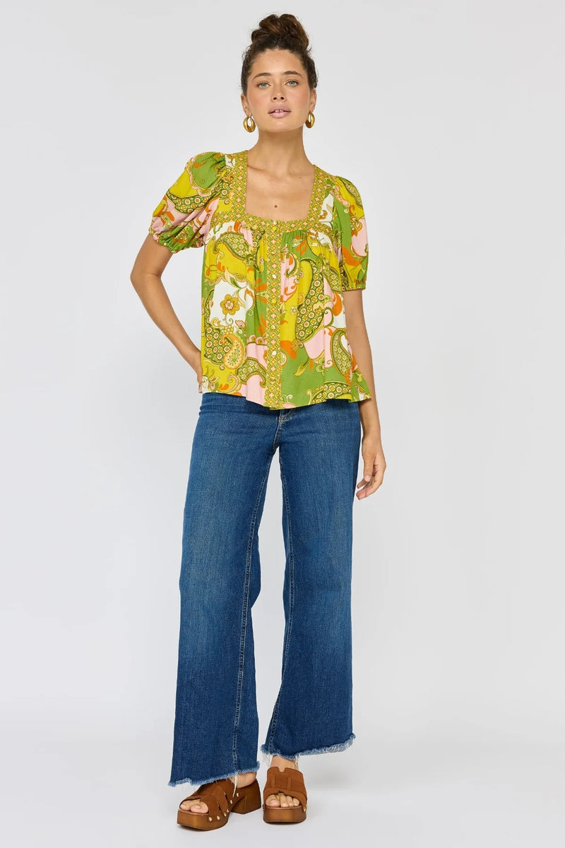 Woman wearing a colorful patterned top and blue jeans on a white background
