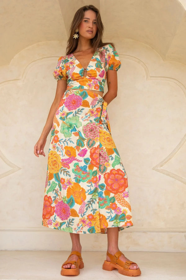 Woman wearing a colorful floral dress against a beige wall.