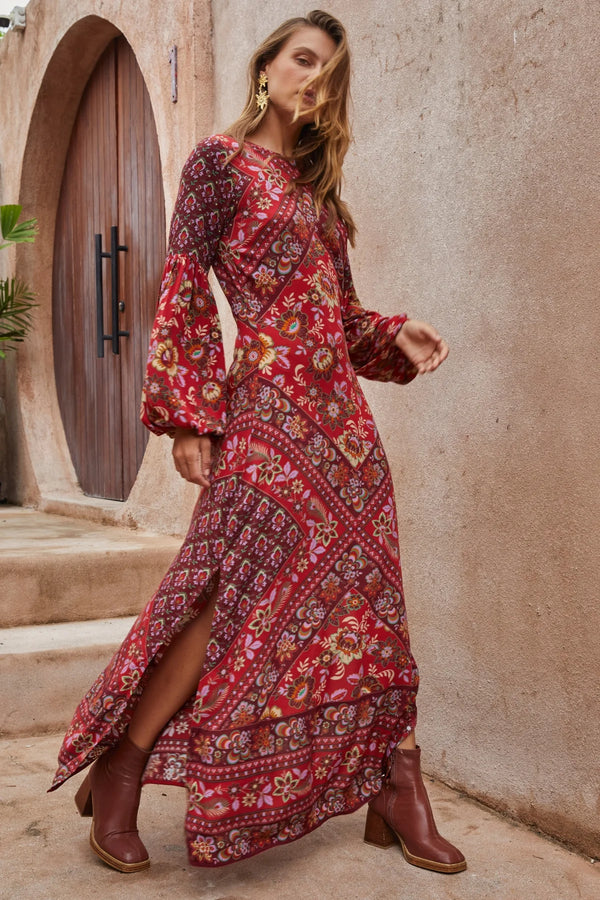 Woman wearing a red patterned dress standing in front of a stone wall.