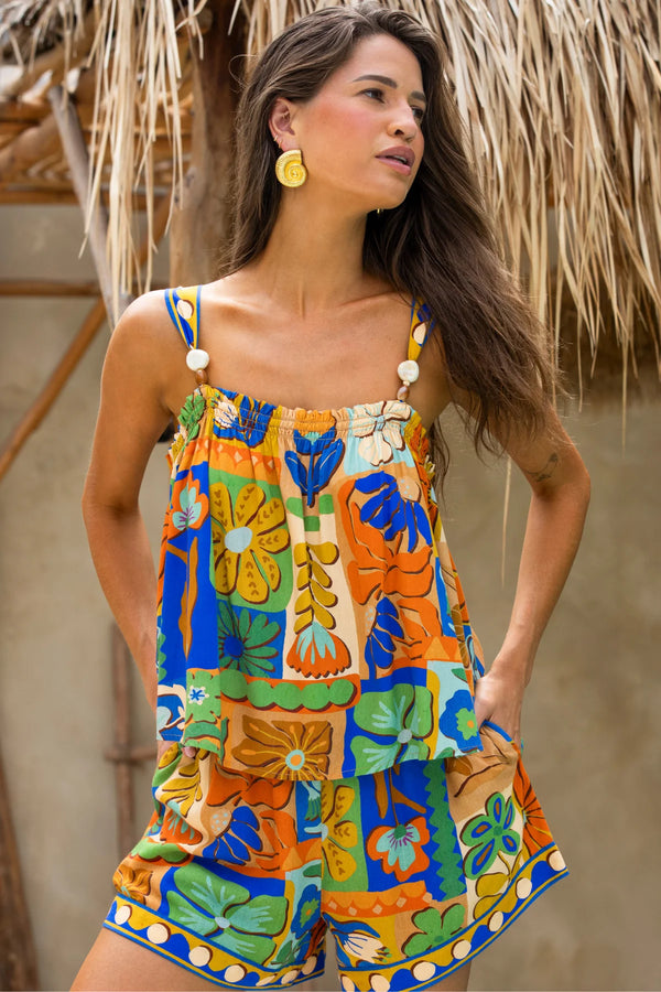 Woman wearing a colorful floral top and shorts with a thatched roof background
