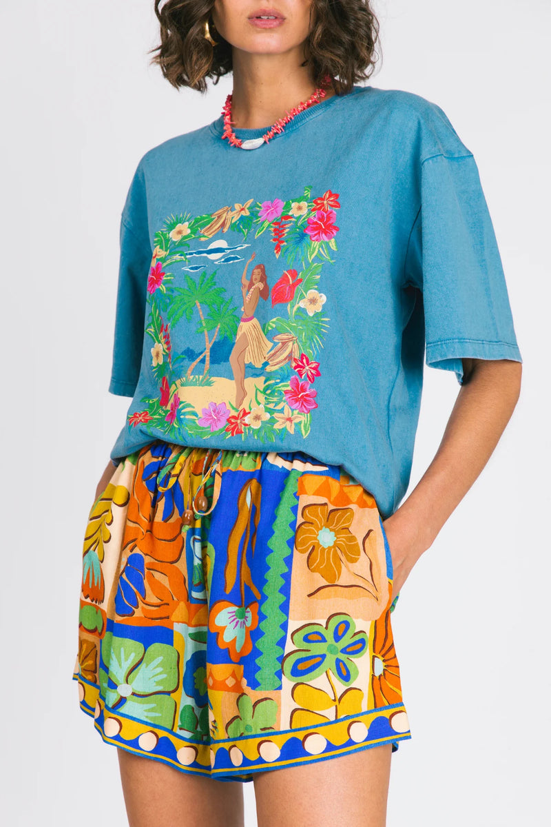 Woman wearing a blue oversized t-shirt with a colorful graphic and a patterned skirt on a white background