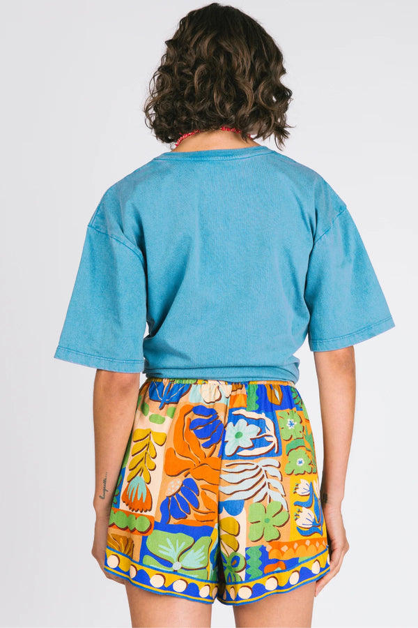 Person wearing a blue crop top and colorful patterned shorts on a plain background