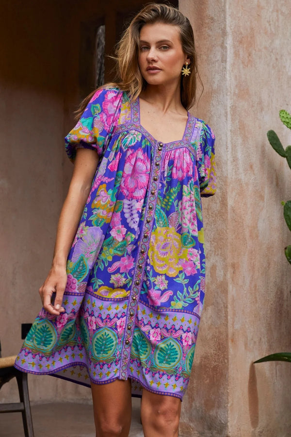 Woman wearing a colorful patterned dress standing against a textured wall.