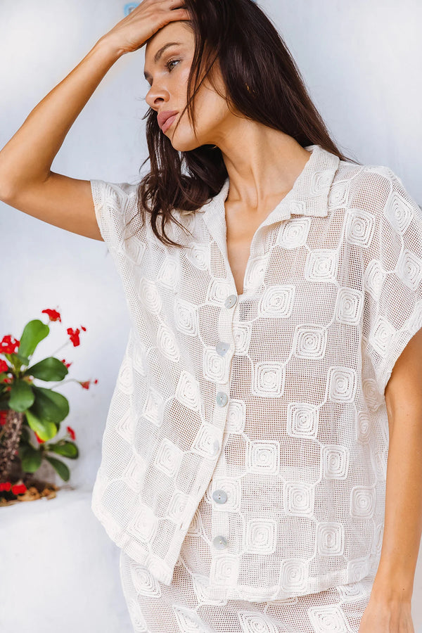 Woman wearing a white patterned shirt against a light background