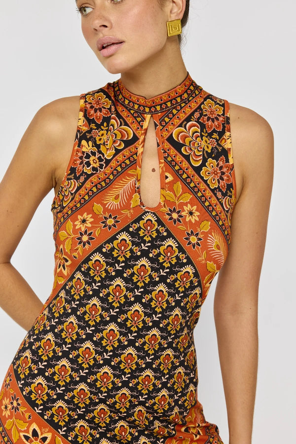 Woman wearing a sleeveless dress with a vibrant pattern on a plain background