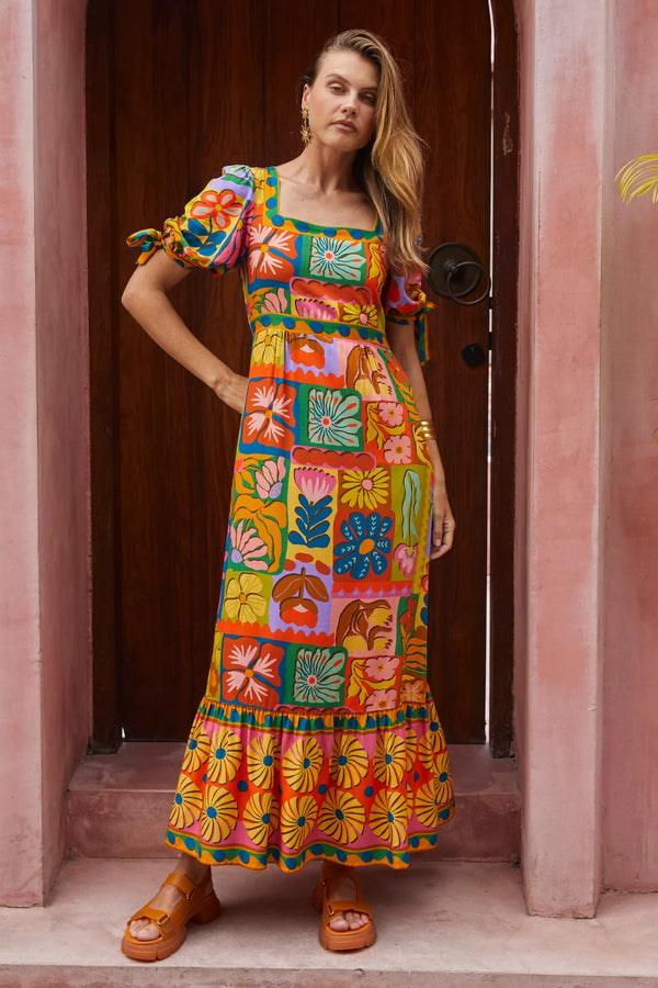 Woman wearing a colorful patterned dress standing in a doorway.