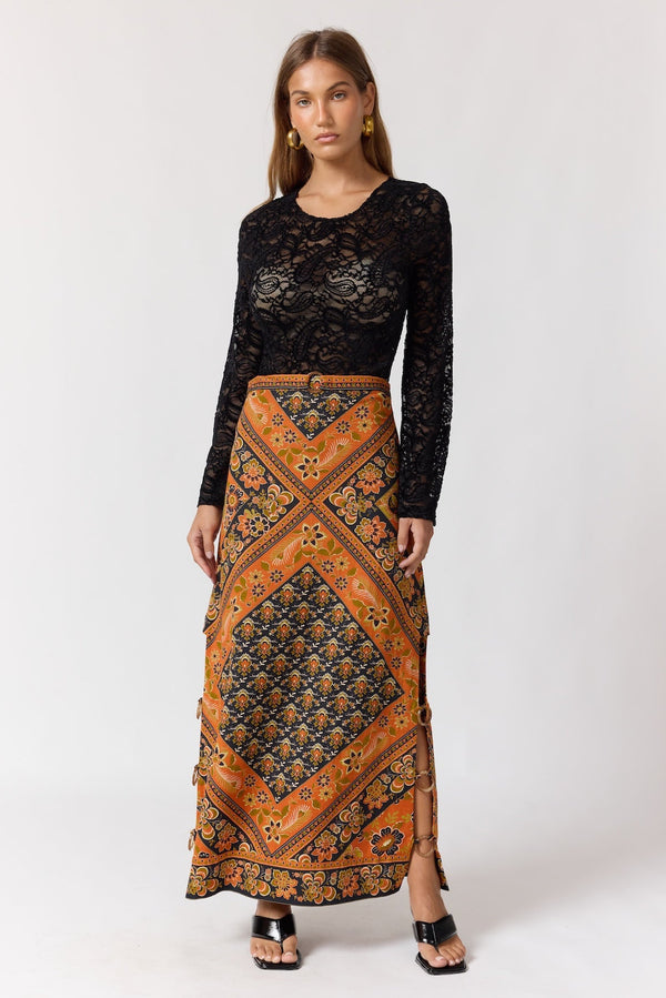 Woman wearing a black lace top and patterned orange skirt on a white background