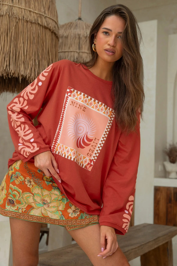 Woman wearing a red patterned top and colorful skirt in a casual setting.