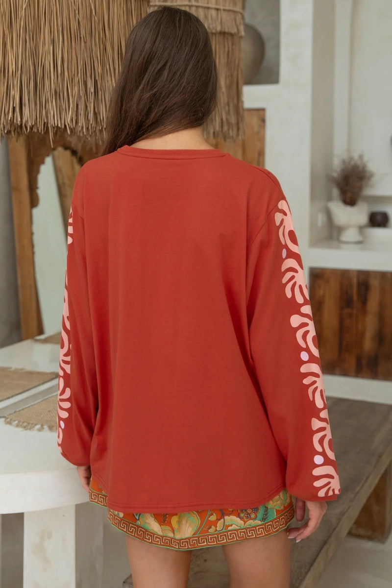 Person wearing a red long-sleeve top with white patterns in a casual setting.