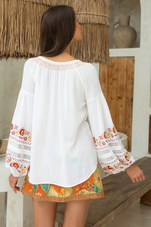 Woman wearing a white blouse with colorful embroidery in a rustic setting