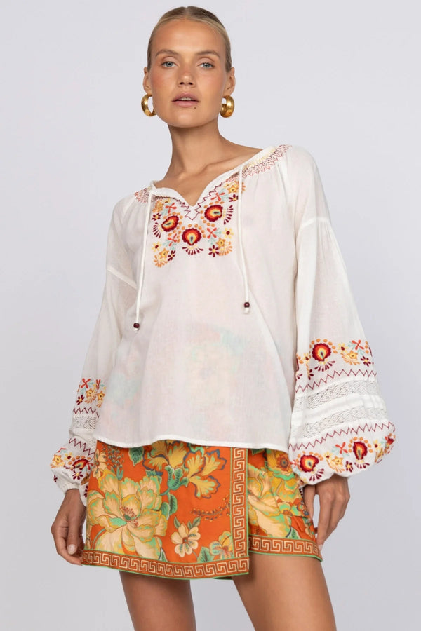Woman wearing a white blouse with colorful embroidery and a patterned skirt on a plain background