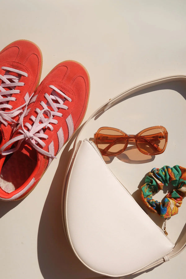 Red sneakers, white handbag with sunglasses and scrunchie on a light background