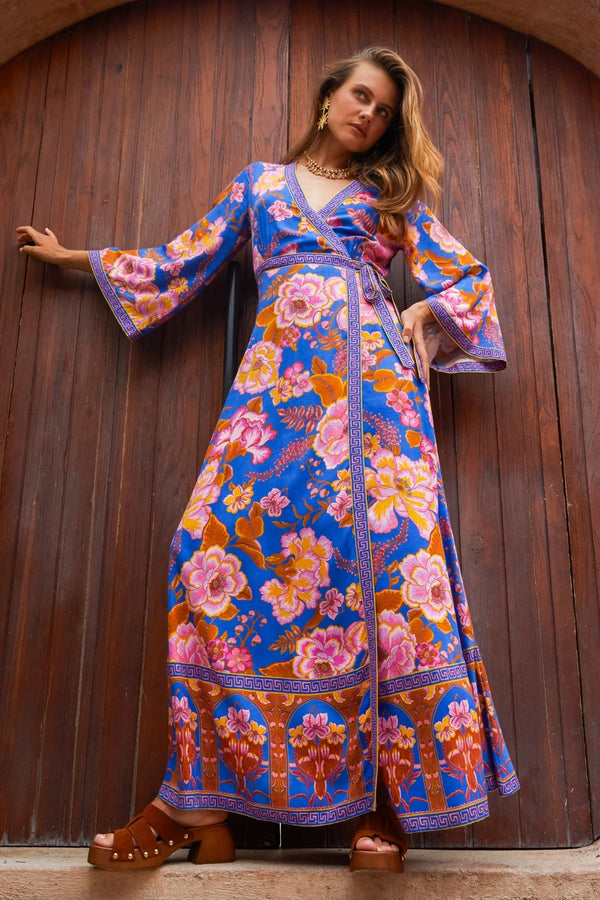 Woman wearing a colorful floral dress against a wooden wall.