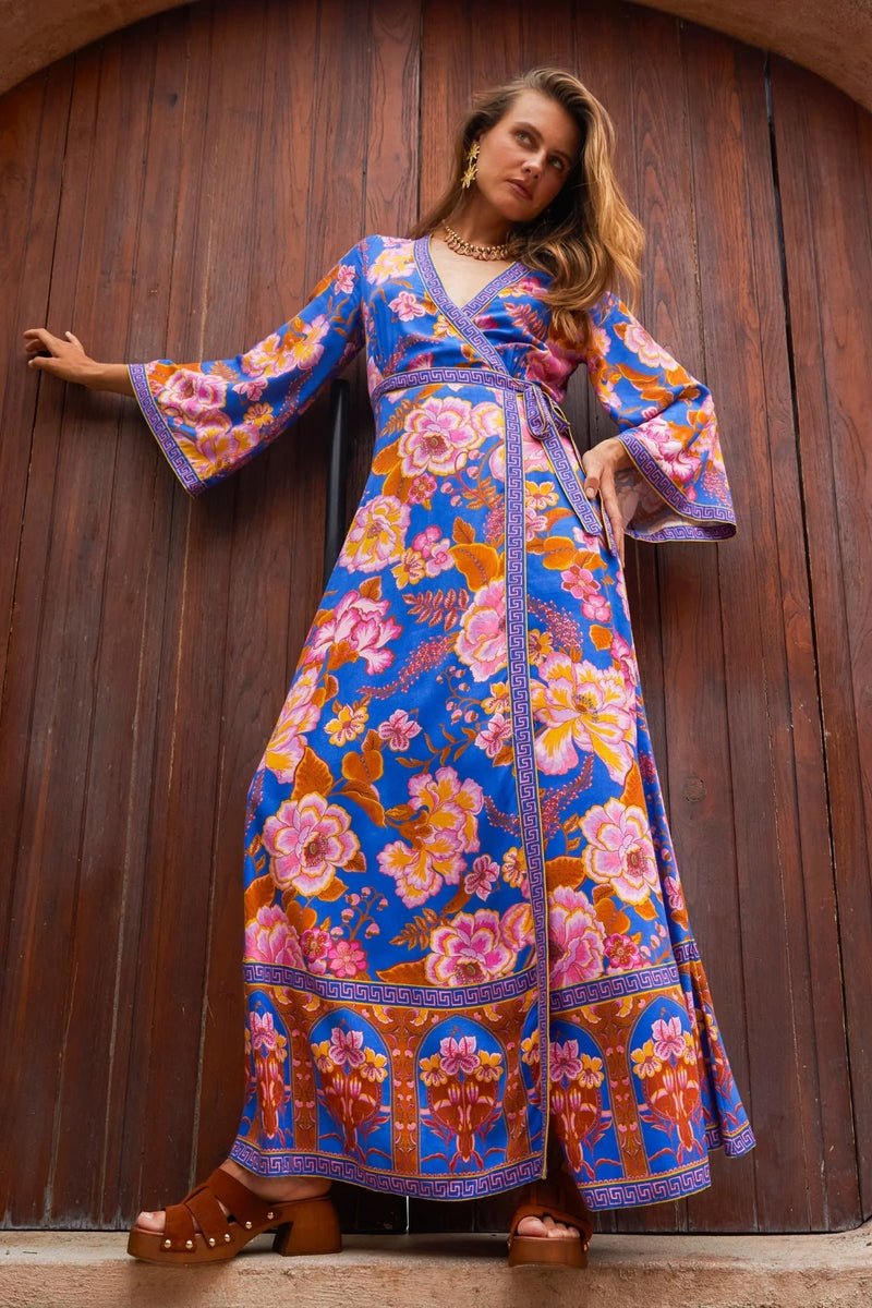Woman wearing a colorful floral dress against a wooden wall.