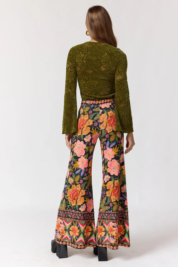 Woman wearing a green top and colorful floral pants on a white background