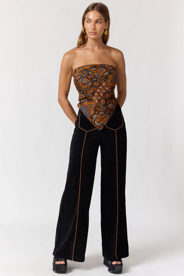 Woman wearing a strapless patterned top and black pants on a white background