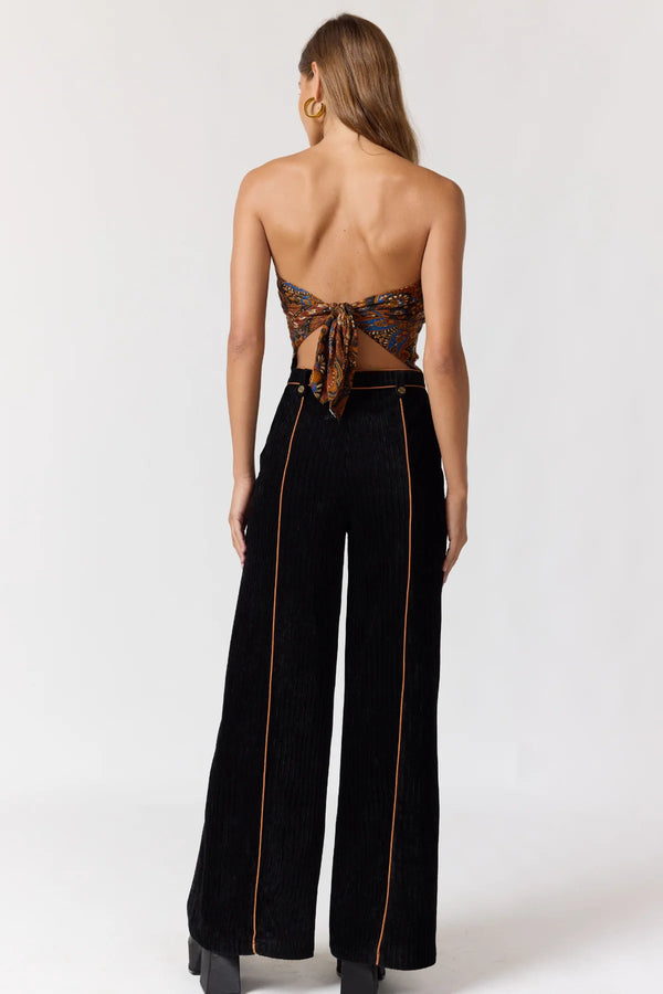 Woman wearing a strapless top with lace-up back and black pants with gold trim on a white background
