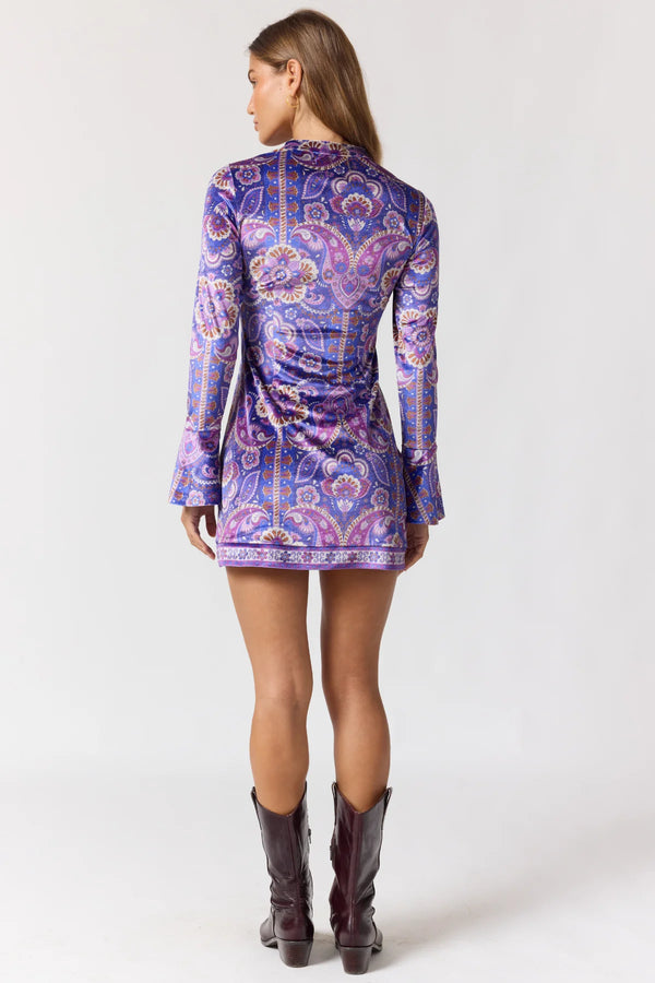 Woman wearing a purple paisley dress with long sleeves on a white background