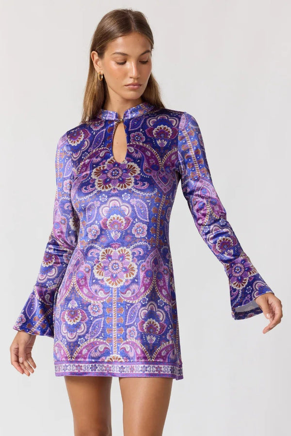Woman wearing a purple patterned dress with long sleeves on a white background