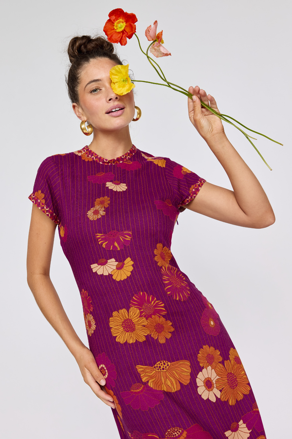 Woman wearing a purple floral dress holding flowers against a white background