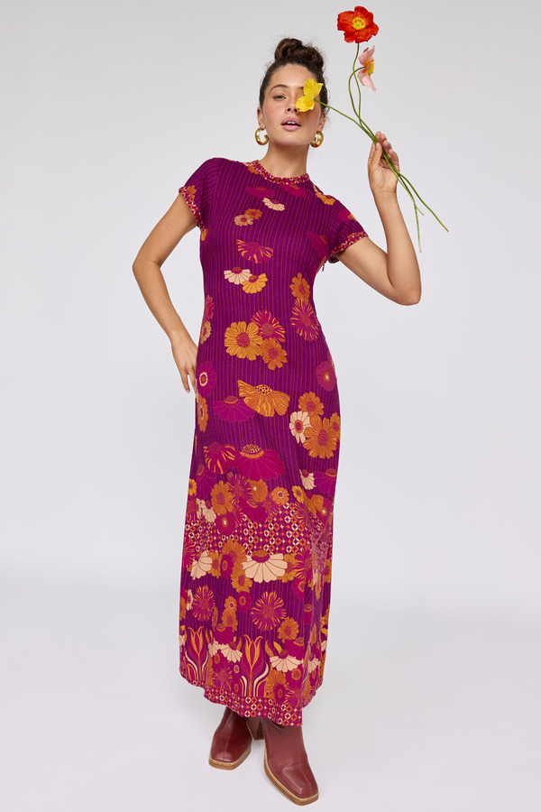 Woman wearing a purple floral dress holding a red flower against a white background