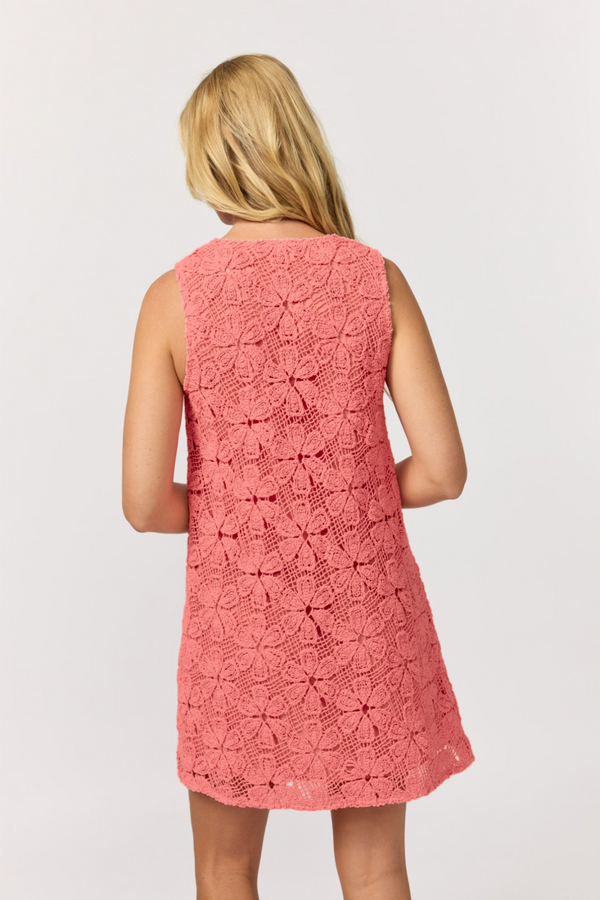A woman modelling a sleeveless pink crochet mini dress with a V-neckline and textured flower crochet pattern.