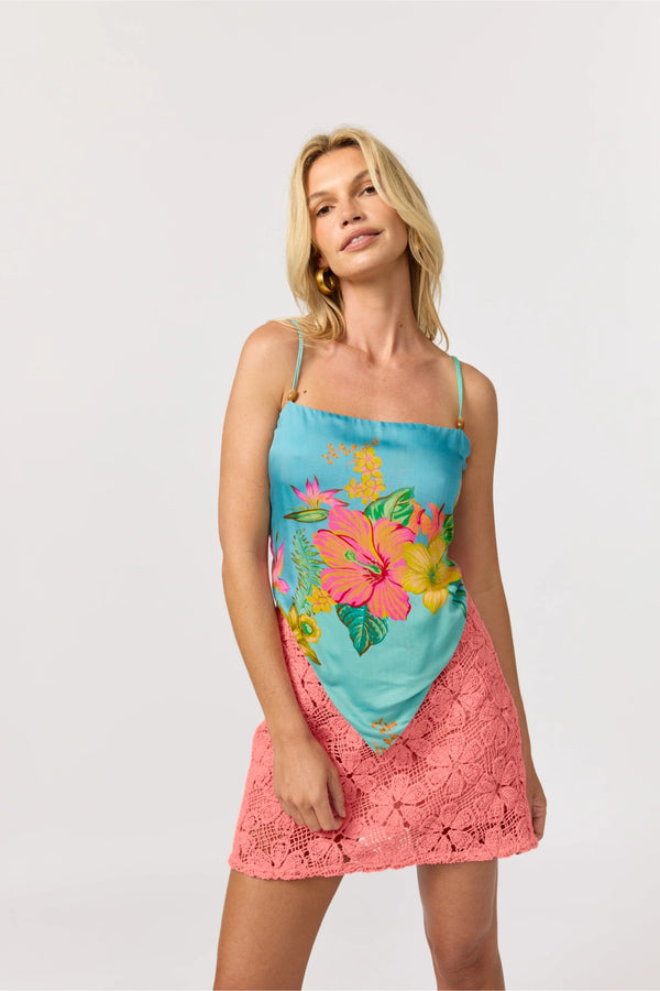 Woman wearing a pink crochet skirt and a turquoise scarf top with colorful floral pattern on a white background