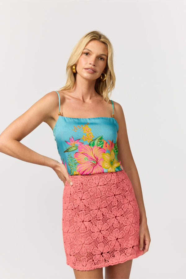 Woman wearing a pink crochet skirt and a turquoise scarf top with colorful floral pattern on a white background